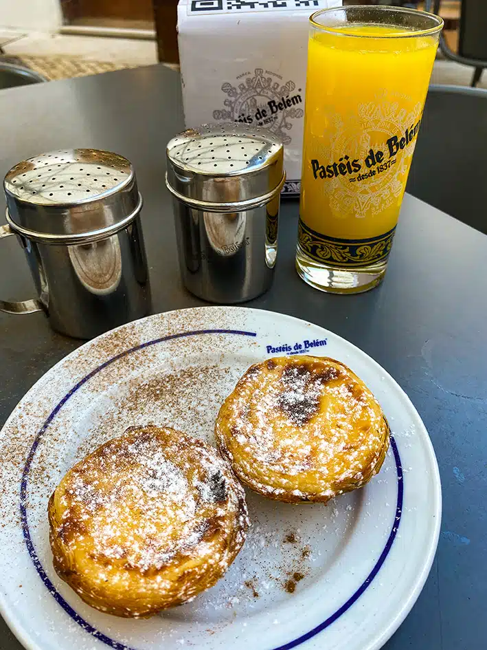 Deux pasteis de Belém saupoudrés de sucre et de canelle dans une assisette, accompagnées d'un jus d'orange dans la célèbre boutique, Pasteis de Belém, à Lisbonne.