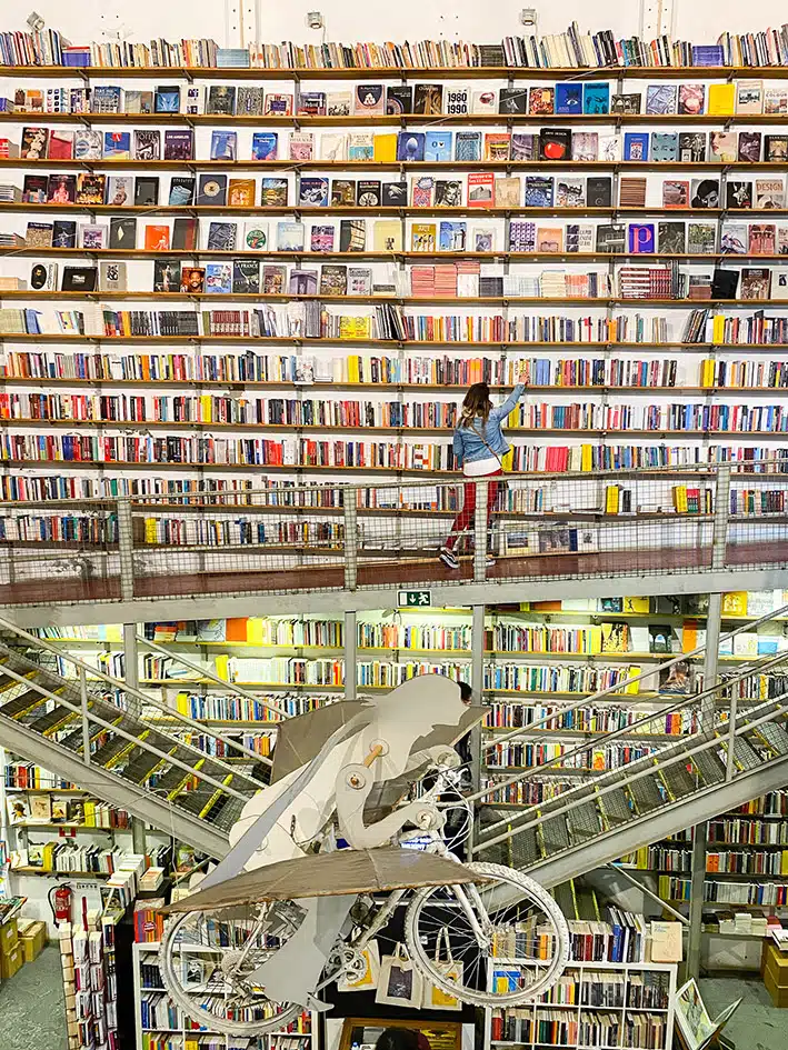 Une jeune femme attrape un livre sur les rayonnages de la librairie Ler Devagar