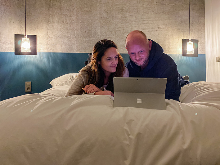 une jeune couple allongé sur un lit regarde un écran d'ordinateur Surface dans une maison d'hôtes en Brabant Wallon