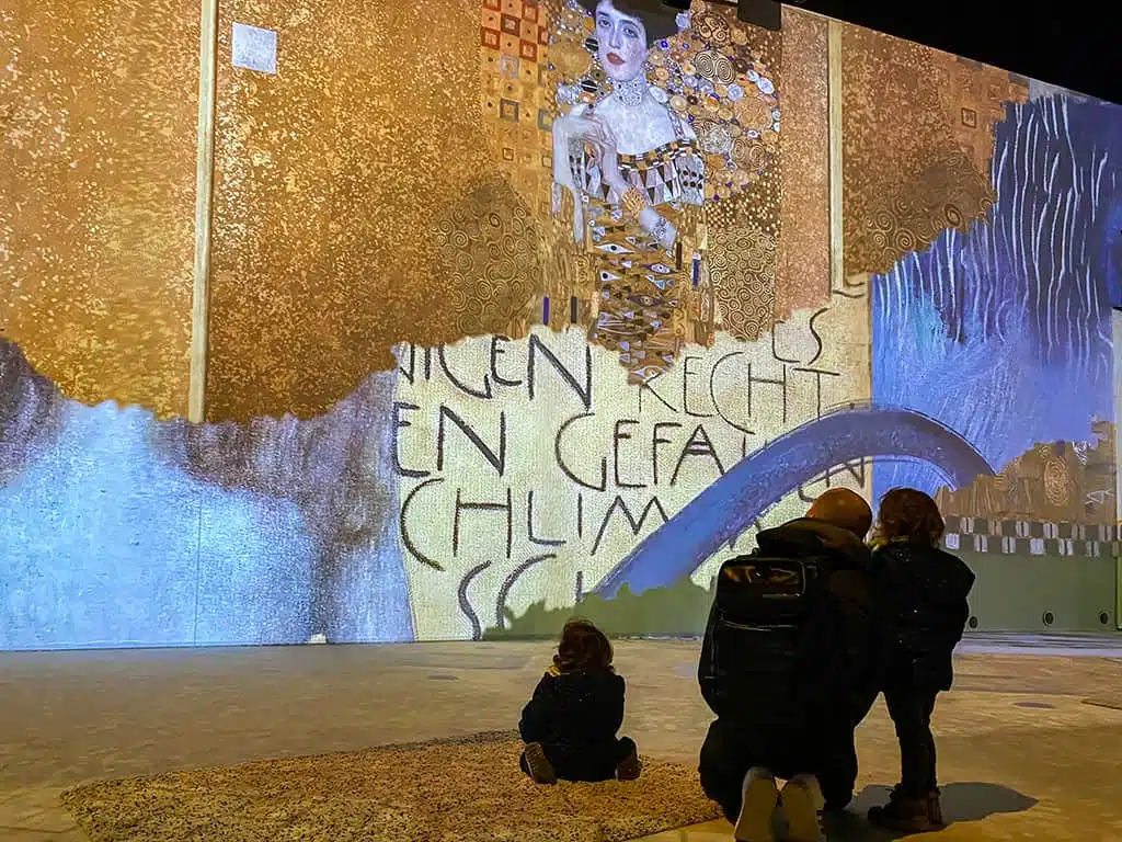 une petite famille installée sur un tapis regarde le show immersif à l'expo Klimt de Bruxelles