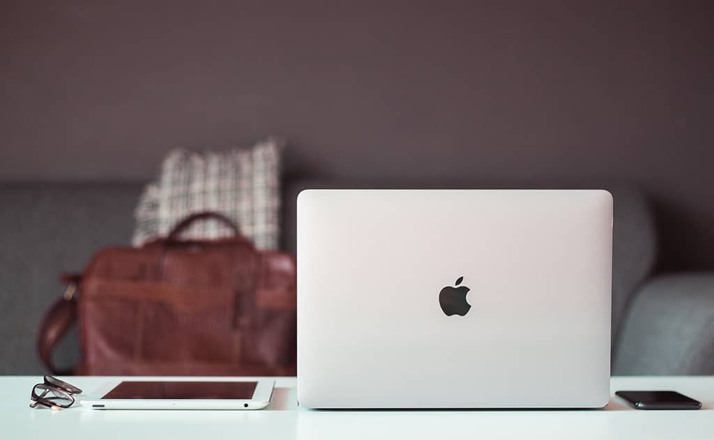 Un bureau blanc avec un ordinateur portable Apple, une tablette et un smartphone. Des outils indispensables pour un nomade numérique