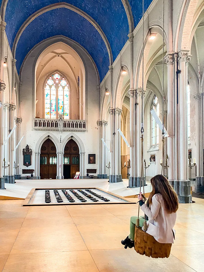 Une jeune femme fait de la balancoire dans l'église Sainte-Madeleine de Bruges. une activité insolite à faire lors d'un city trip à Bruges.