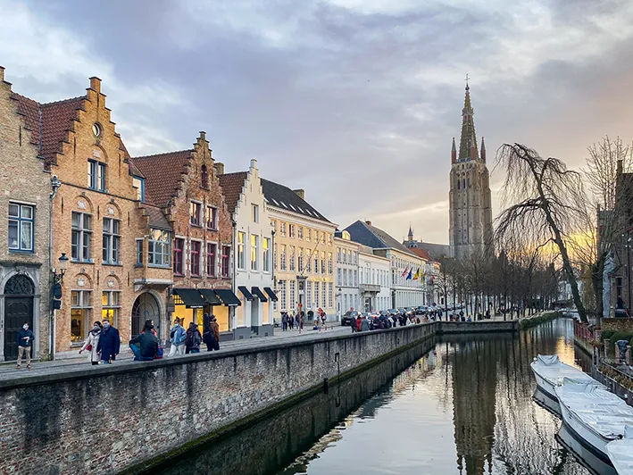 Un canal à Bruges avec des maisons séculaires et en arrière plan la tour de l'église Notre-Dame lors d'un week-end en amoureux à Bruges