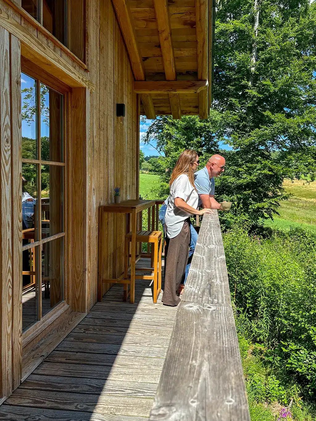 Un couple profite d’un moment paisible sur le balcon en bois du Woodpecker Lodge, en pleine nature, lors d’un week-end romantique en Ardennes.