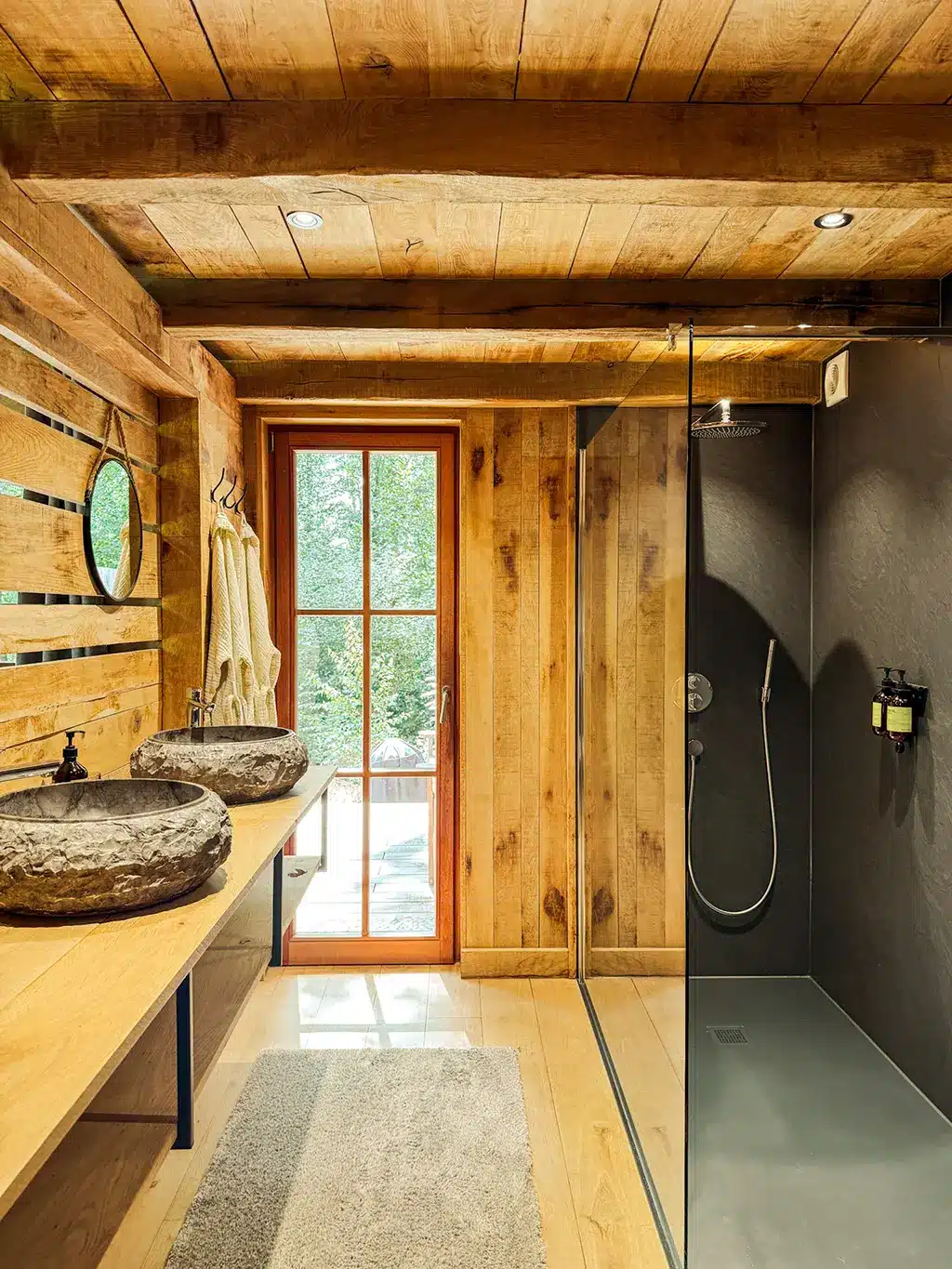 Salle de bain lumineuse et naturelle du Woodpecker Lodge avec douche italienne et vasques en pierre, parfaite pour un week-end romantique en Ardennes.