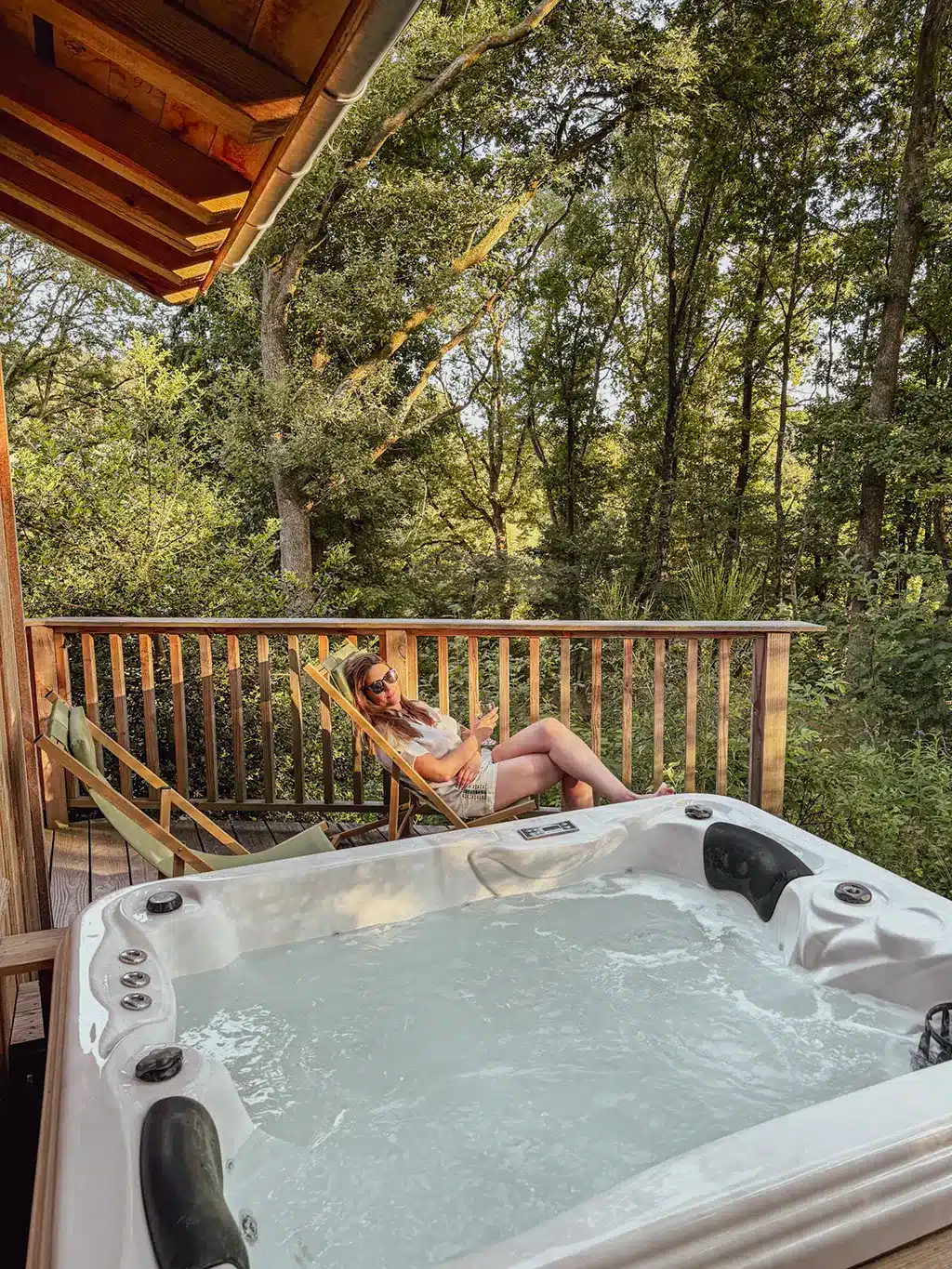 Femme détendue sur un transat devant un jacuzzi sur une terrasse en bois, entourée de forêt en Ardenne.