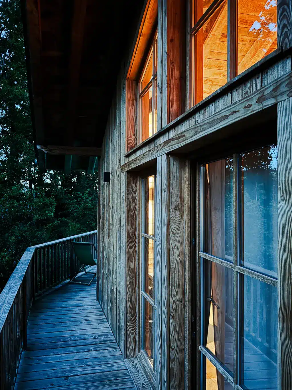 Balcon en bois longeant le chalet, ambiance chaleureuse au crépuscule.