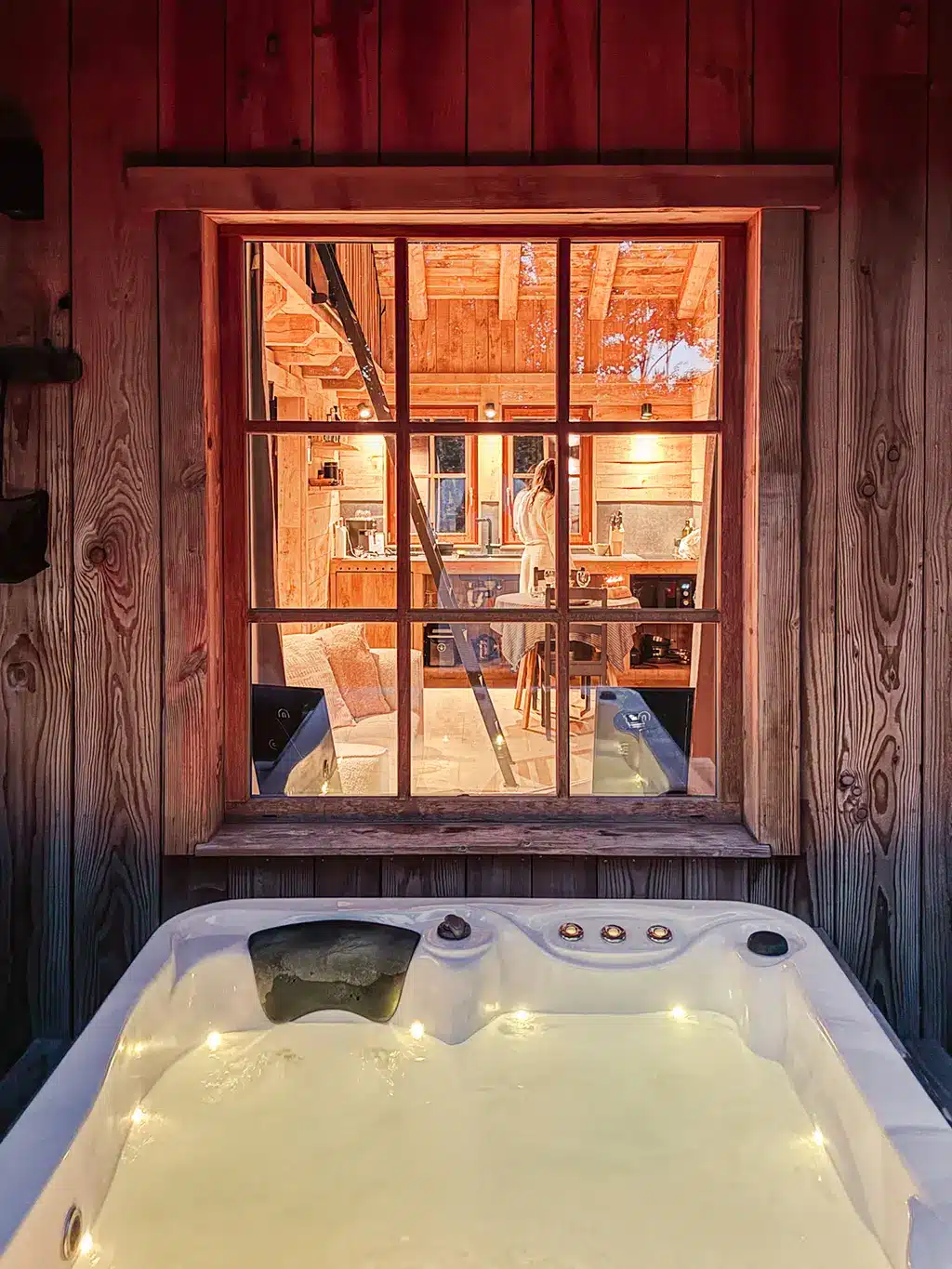 Vue sur l’intérieur du chalet depuis le jacuzzi, lumière tamisée et atmosphère cosy.