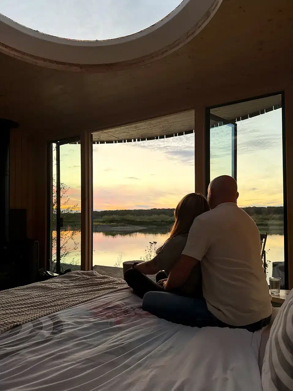 Couple installé sur le lit de la cabane face au coucher du soleil