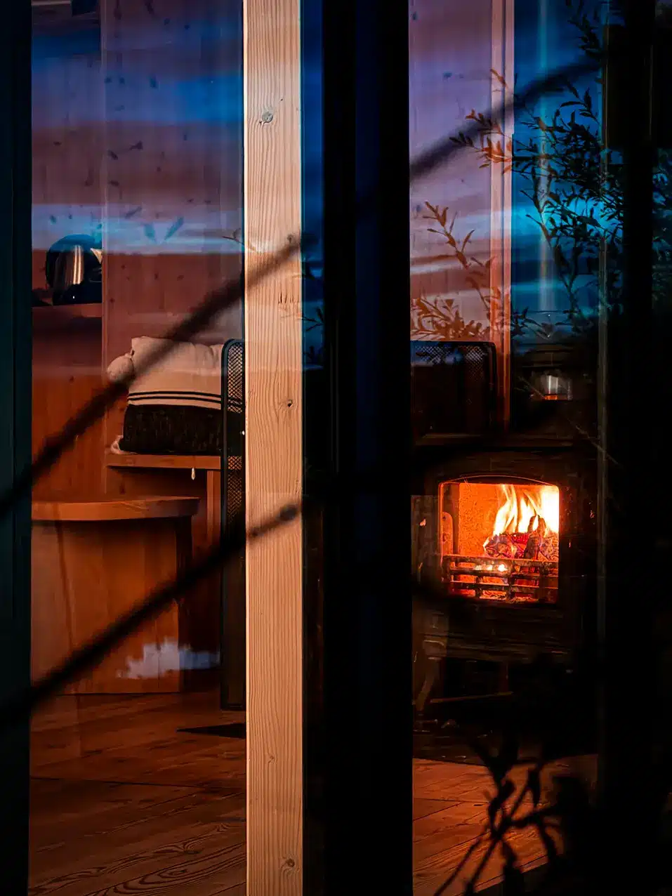 Flammes du poêle à bois visibles à travers la baie vitrée de la cabane
